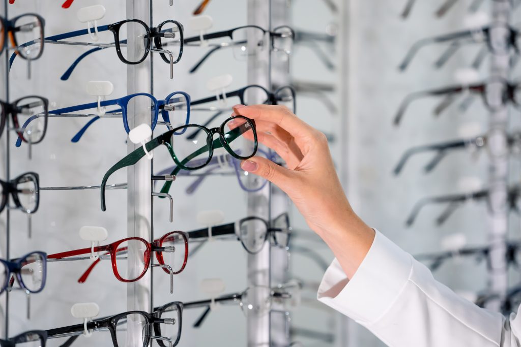 Row Of Glasses At An Opticians. Eyeglasses Shop. Stand With Glasses In The Store Of Optics. Woman's Hand Chooses Glasses
