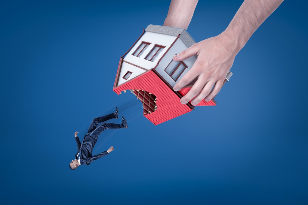 Close Up Of Man's Hands Holding House With Hole In Roof Upside Down And Dropping Out Little Businessman.