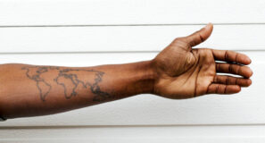 Mà jove d'una persona immigrant amb un tatuatge del mapa del món